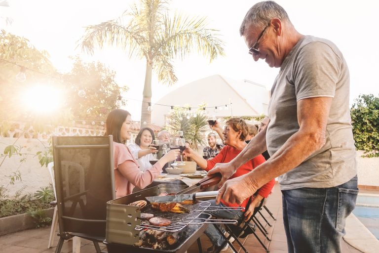 Happy family cheering and toasting with red wine in barbecue party - Chef senior man grilling meat and having fun with parents - Weekend food bbq and reunion young and older people lifestyle concept